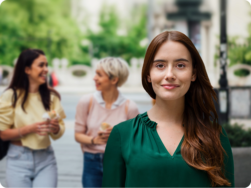 Smiling woman in a green blouse, with two women talking in the background